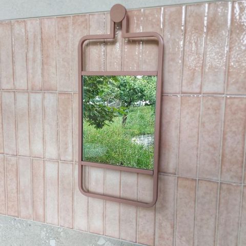 Rechteckiger Spiegel mit rosafarbenem Metallrahmen an einer gefliesten Wand, zeigt Garten mit Pflanzen