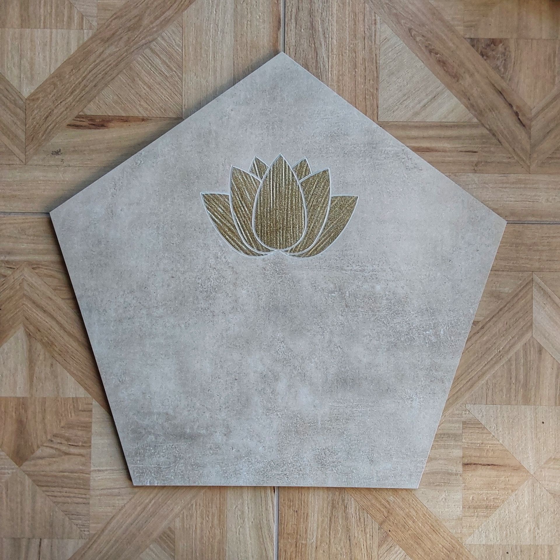 Fünfeckige graue Steinplatte mit goldener Lotus-Blüte, auf Holzboden mit geometrischem Muster